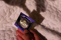 Hand holding a SKYN condom sleeve over a bed