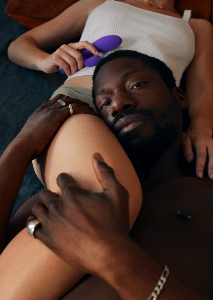 Man leaning his head over the thigh of a girl holding a SKYN Vibes sex toy