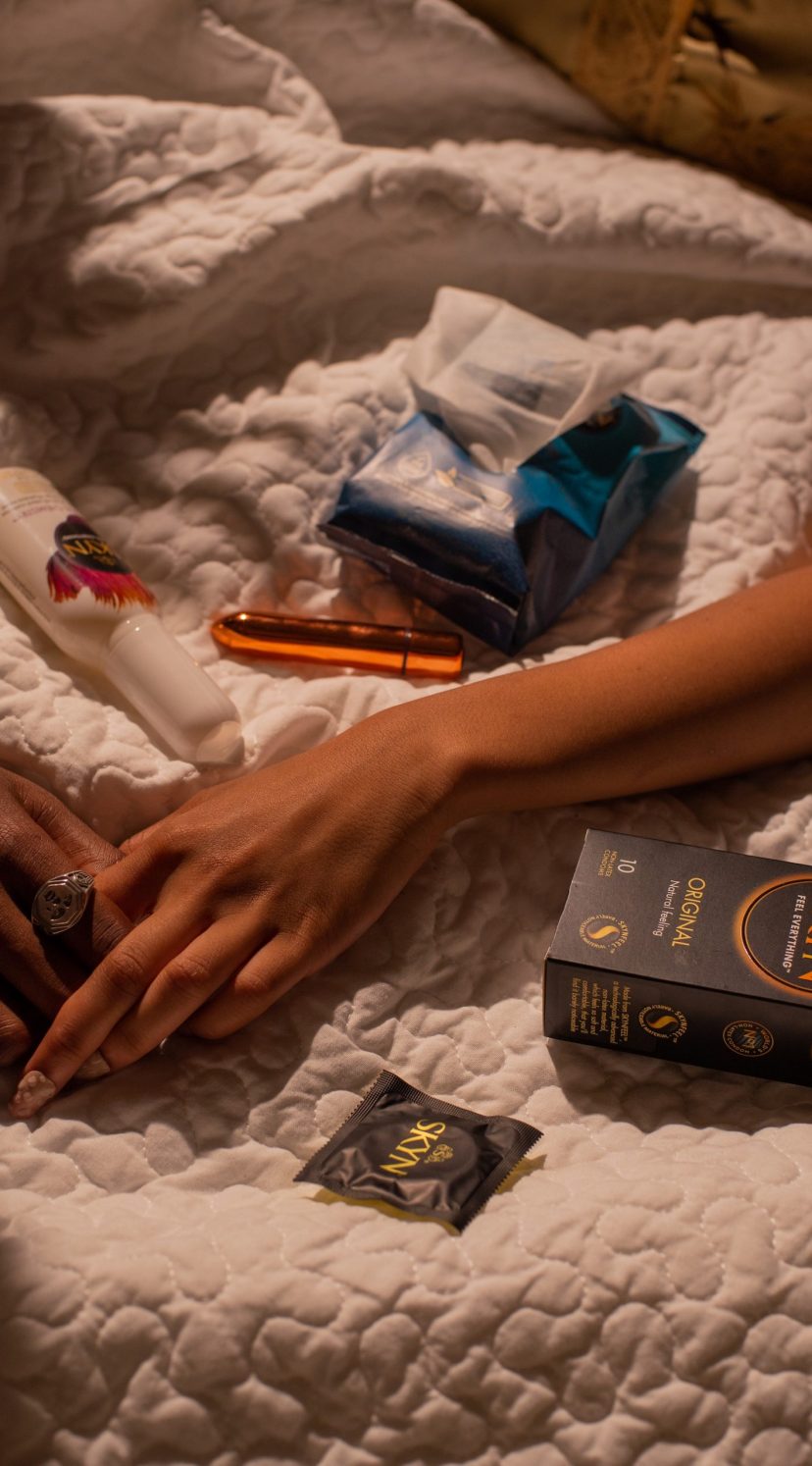 Man hand holding woman hand with SKYN products lying around on a bed