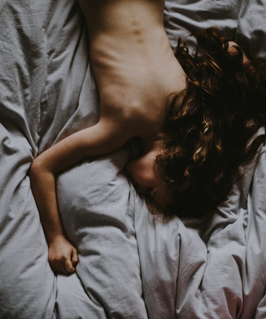 A naked girl laying in gray bedsheets