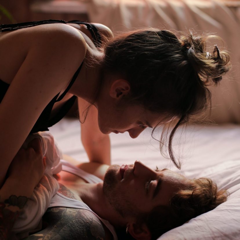 A girl on top of a her man in bed and about to kiss